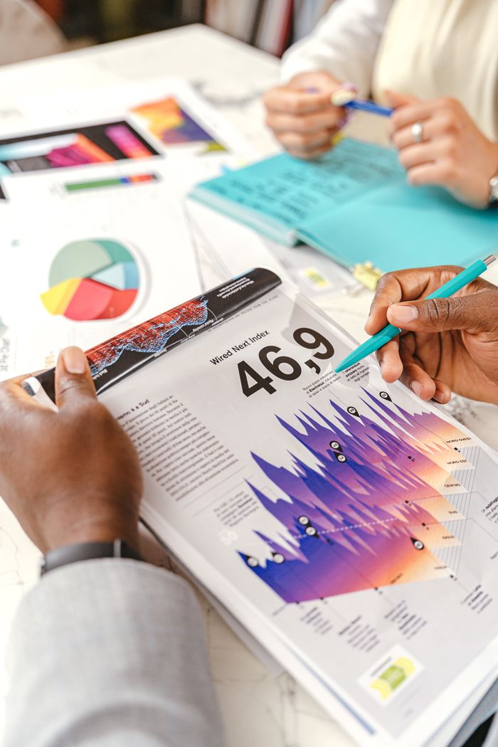 who-we-are Hands discussing vibrant data charts during a business meeting, with papers and diagrams.